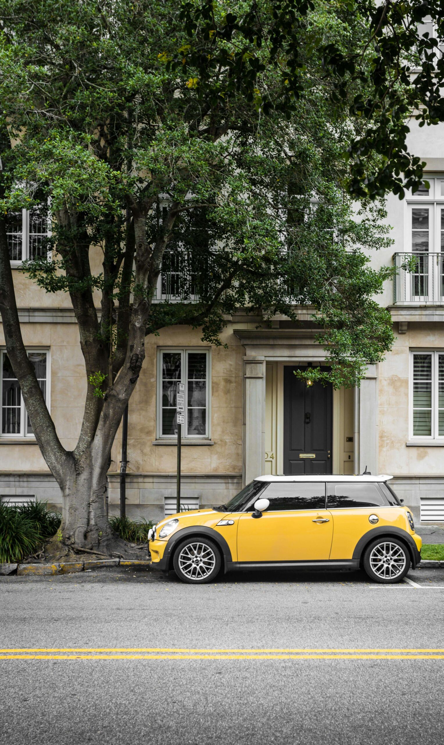 Sárga Mini Cooper parkol egy városi ház előtt nagy fával