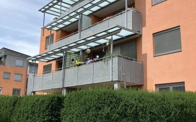 Narancssárga társasház üveg előtetős erkélyekkel és magas zöld sövénnyel